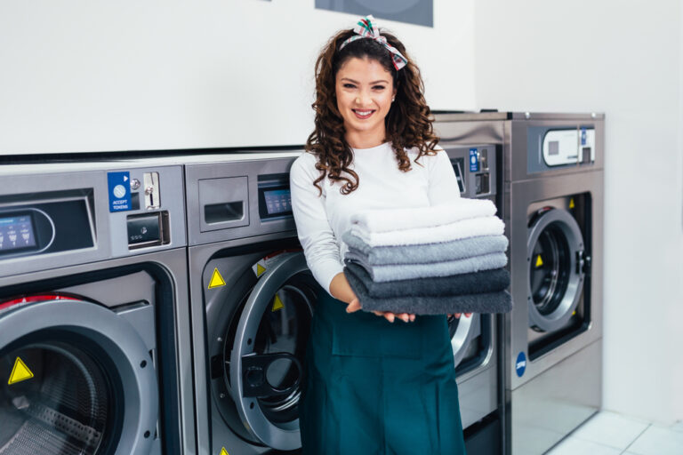 Smiling staff member holding folded laundry at a professional laundromat